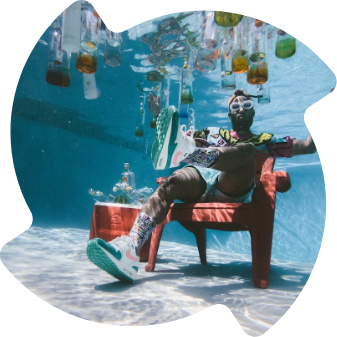 Bunt gekleideter Mann mit Sonnenbrille im Sessel unter Wasser
